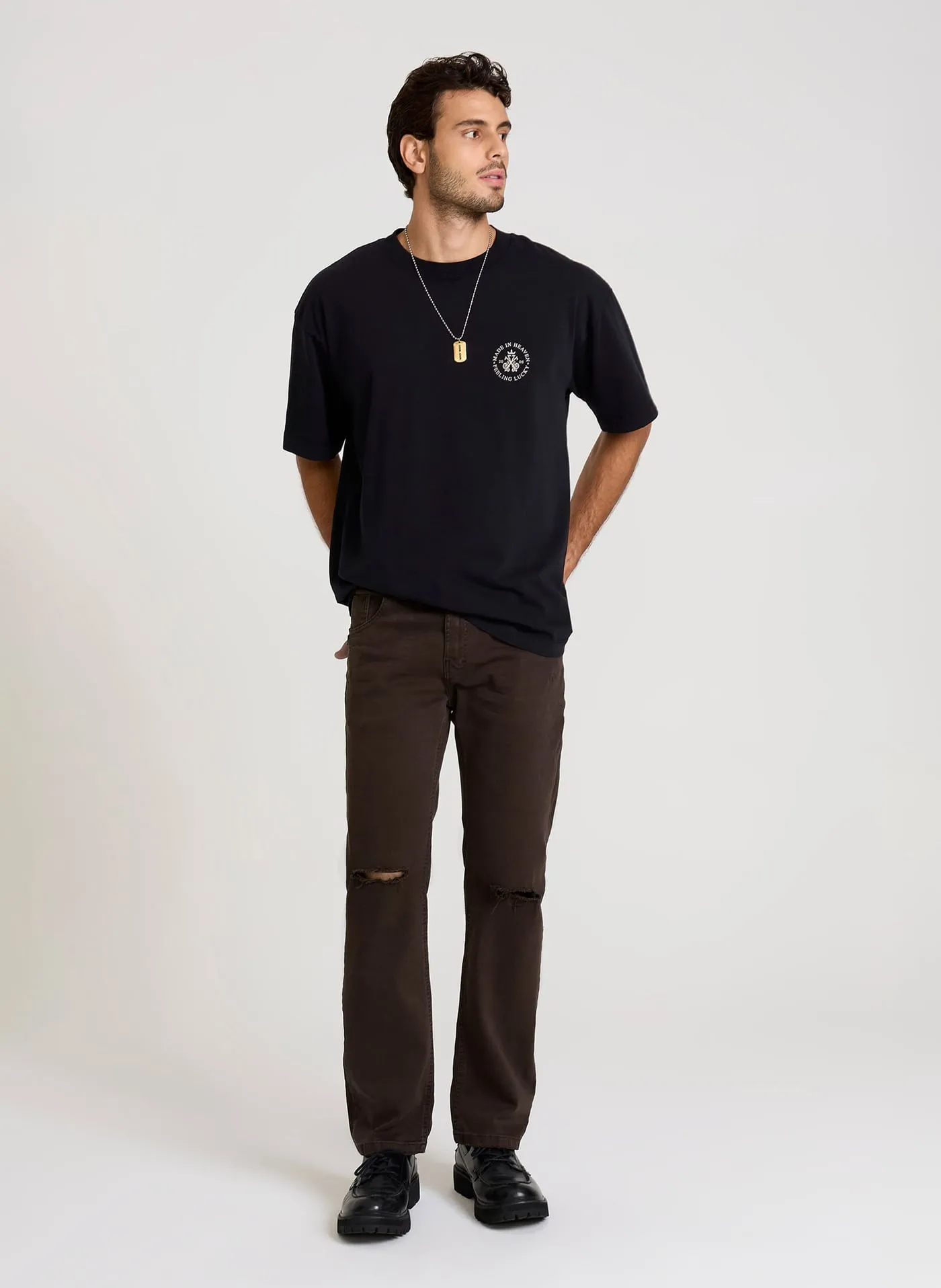 Modelo com camiseta preta e calça marrom com rasgo no joelho